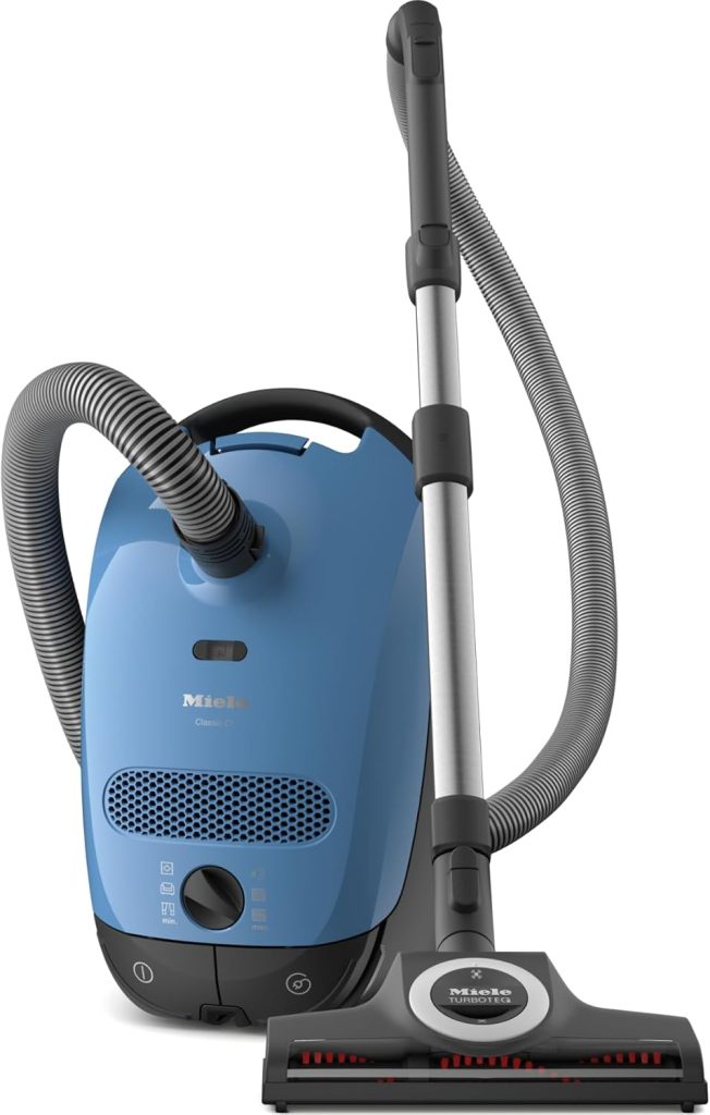 
Miele Classic C1 Turbo Team PowerLine vacuum cleaner with a sleek canister design, equipped with a TurboBrush and multiple cleaning attachments, positioned in a stylish home environment for effective cleaning of hard floors and carpets.