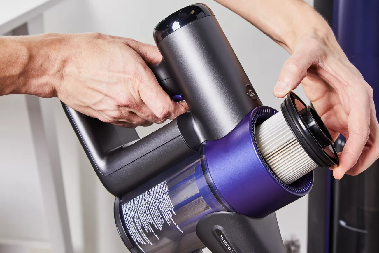 Close-up of hands removing the filter from a cordless vacuum cleaner, highlighting its maintenance process.