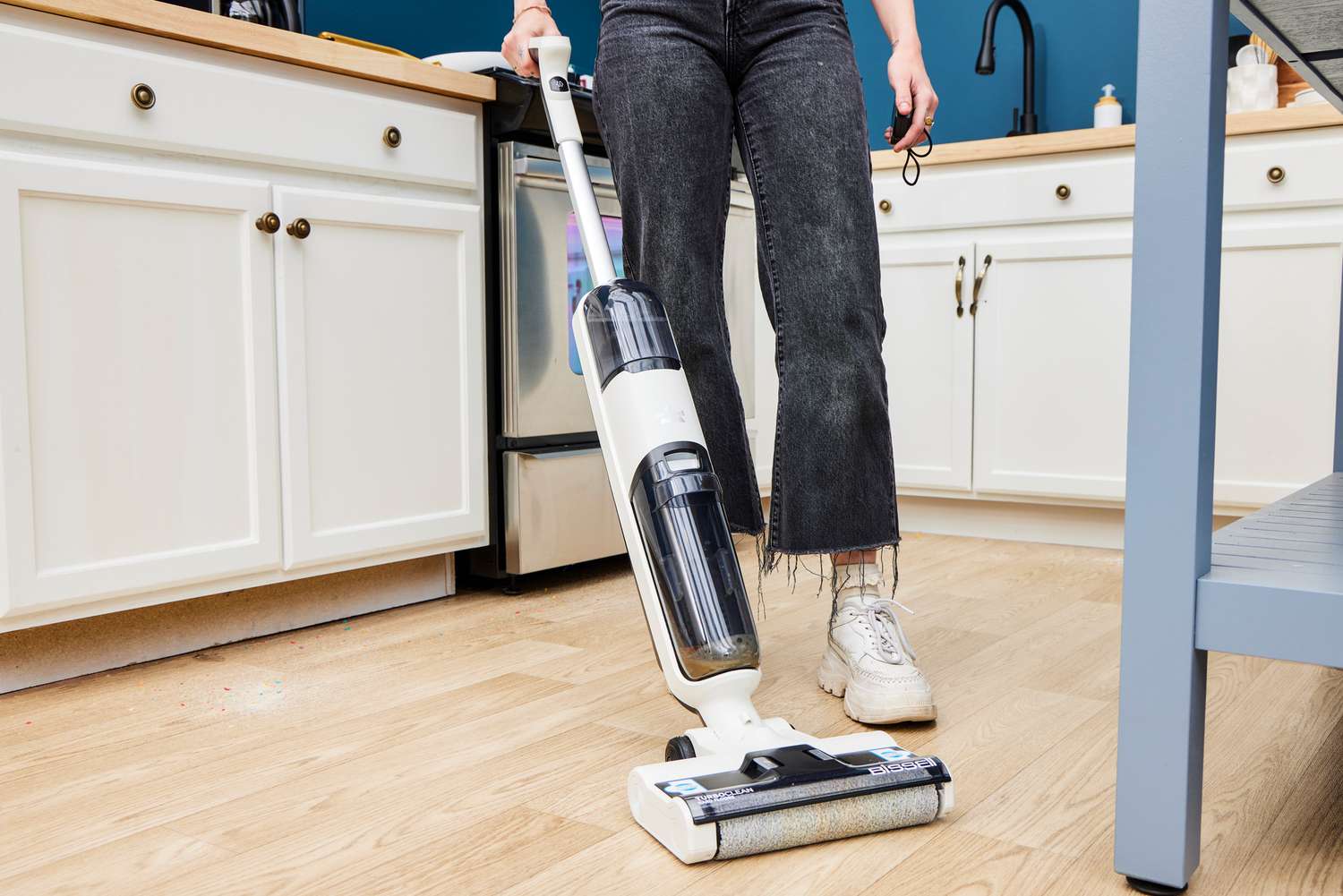 Person using a Bissell TurboClean cordless vacuum mop on a hardwood kitchen floor, with white cabinetry and a modern kitchen background.